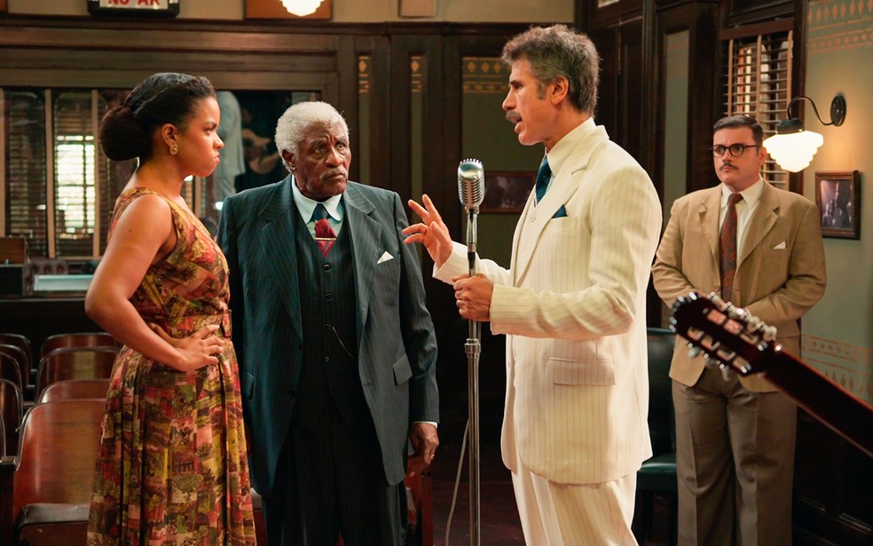 Ernesto (Eriberto Leão) tenta impedir Dita (Jeniffer Nascimento) de cantar na rádio - Êta Mundo Melhor! — Foto: Globo