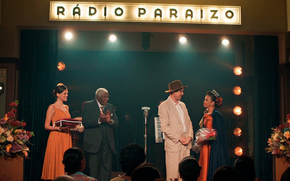 Candinho (Sergio Guizé) surpreende Dita (Jeniffer Nascimento) durante coroação em concurso na rádio Paraízo - Êta Mundo Melhor! — Foto: Globo